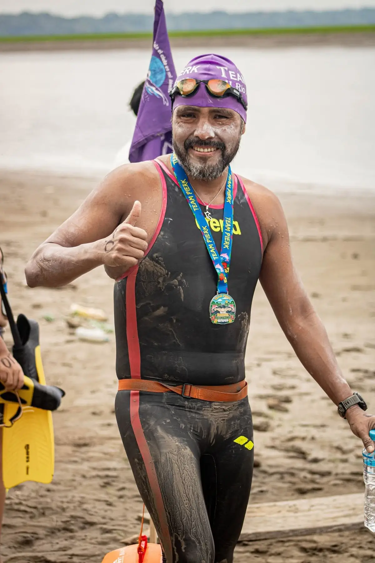 Carlos com a medalha ao pescoço, o polegar para cima e o rosto ainda sujo de lama