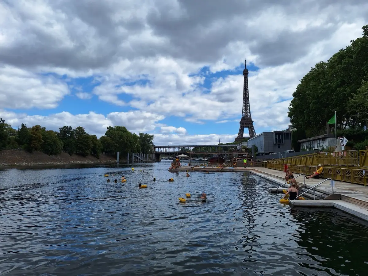 Banhistas com boias amarelas num tanque criado no Sena, com a Torre Eiffel no centro do enquadramento