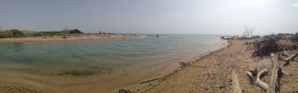 Panorama da foz de um rio siciliano: a curva de água doce fechada por uma língua de areia, e para lá da areia o mar aberto
