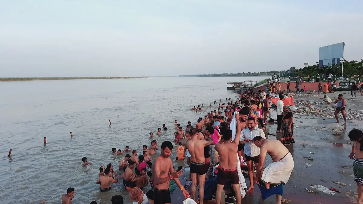 Centenas de pessoas na água na margem do Ganges num dia de festa, com os resíduos acumulados na areia em primeiro plano